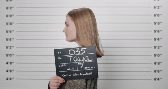 Mugshot of Arrested Female Person Holding Sign While Being Photographed in Front of Metric Lineup