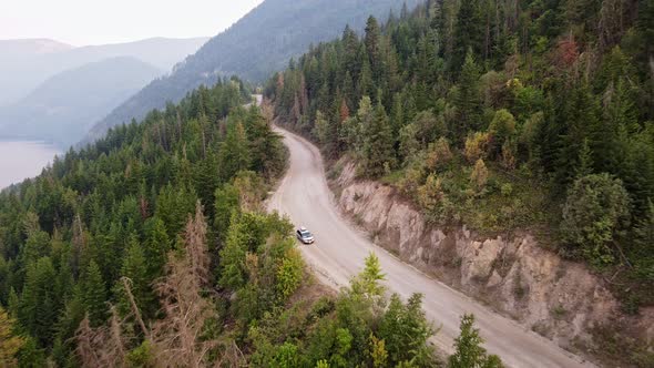 Silver van parked along a dusty forest service road during wildfire season with Adams Lake in the ba