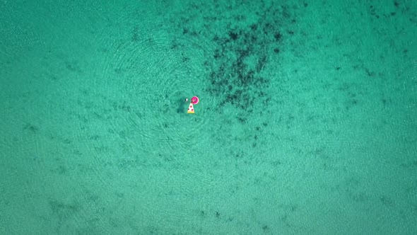 High aerial view of two young girls swimming and playing in sea with inflatables.