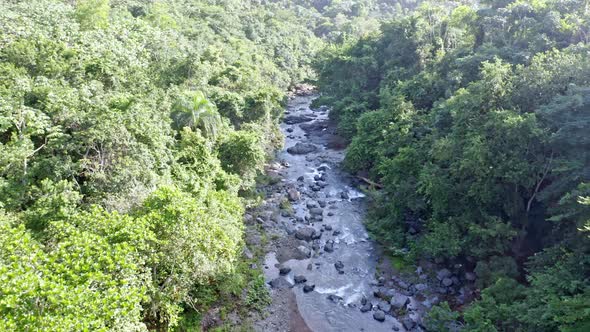 Higuero creek running through rocks in green forest, La Cuaba in Dominican Republic. Aerial forward