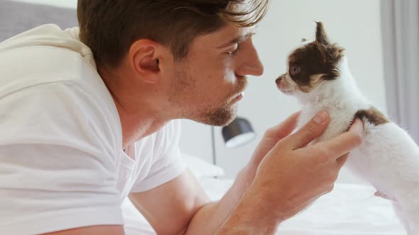 Happy young man lying on bed stroking his puppy in the bedroom 4K 4k