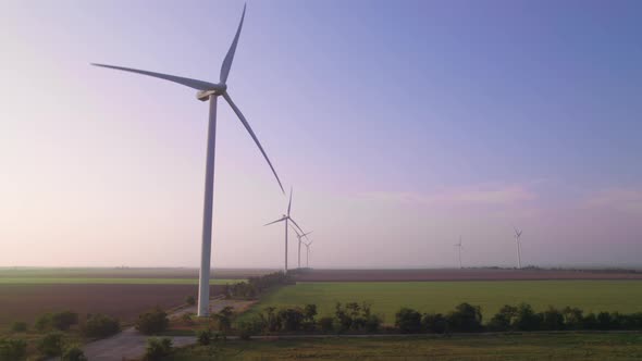 Windmills in a green field at sunset. Wind farm with turbine cables for wind energy.