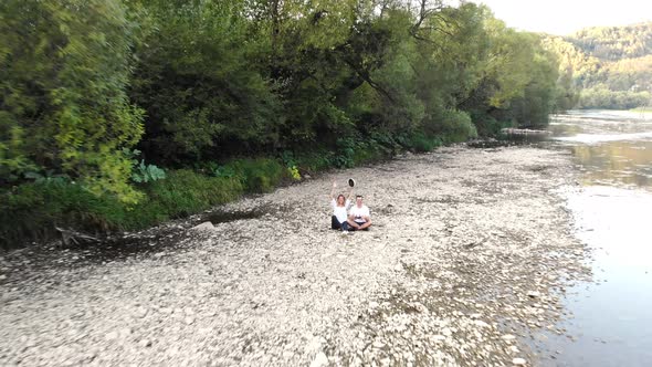 Pull Away Aerial Shot of Couple Sitting on Bank of Stream and Enjoy Majestic Nature View