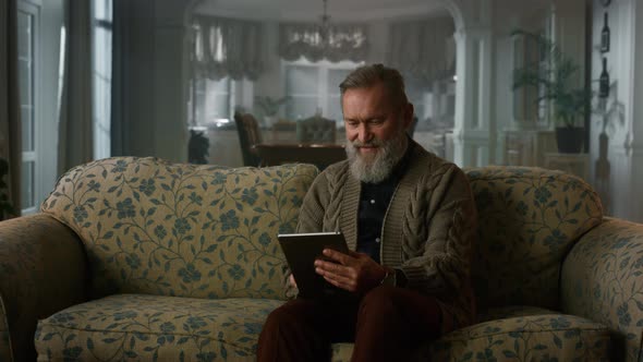 Calm Senior Man Using Tablet Computer on Sofa