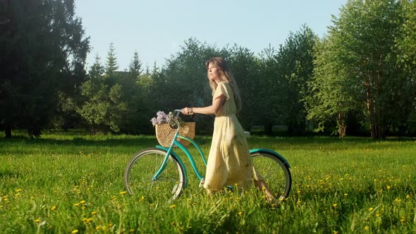 Happy Young Woman Walk With a Bike With Basket of Flowers on the On Countryside Road At Summer at