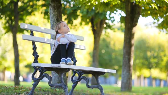 Cute Kid Sitting Lost in Thought at Beautiful Autumn Day Outdoors. Little Girl on the Bench in Fall