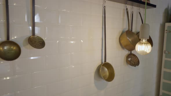 Handheld Pan Along Metal Pots Hanging on White Tile Kitchen Wall