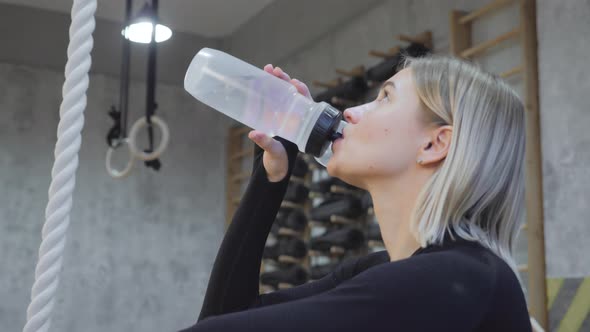 Close-up of a Young Blonde Athletic Woman Drinking Water from a Bottle After an Exercise