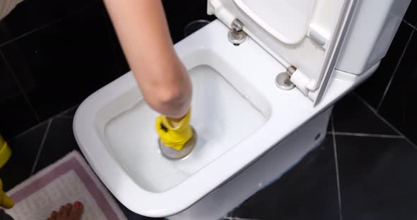 A Woman in Yellow Gloves Washes the Toilet with a Brush