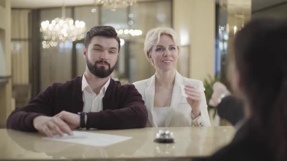 Portrait of Positive Caucasian Man Signing Documents As His Spouse Taking Room Key Card From