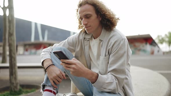 Handsome curly-haired man texting by phone