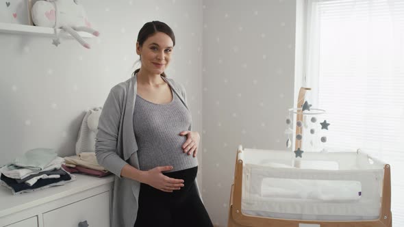 Thoughtful caucasian woman in advanced pregnancy standing in the baby's room next to the crib. Shot