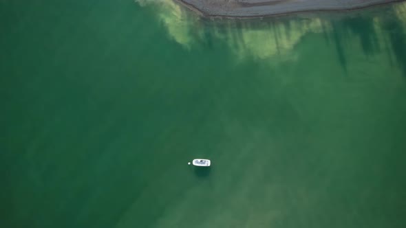 Drone ascending revealing little speedboat still close to little island on turquoise water reservoir