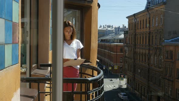 Portrait of Young Woman Drawing With Pencil In Album on Balcony in Downtown