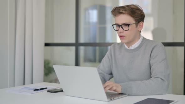 Young Man Coughing While Using Laptop in Modern Office