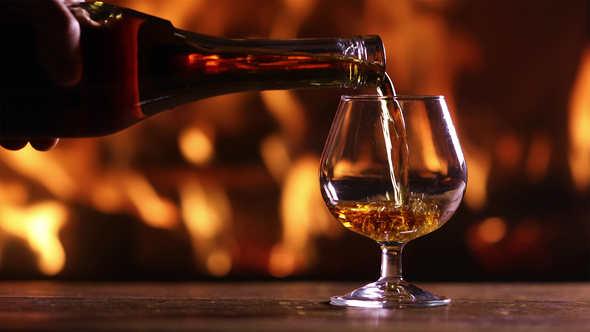 Man's Hand Pours Brandy Into a Glass