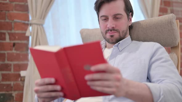 Portrait of Casual Young Man Reading Book on Sofa