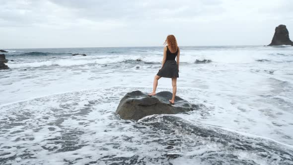 Woman in Dress Standing on a Big Rock on the Shore of the Black Volcanic Black Sand Beach Benijo in