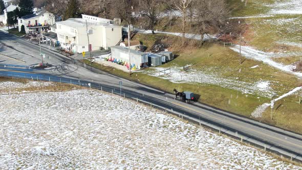 AERIAL Horse-Drawn Carriage Trotting Into Rural Township While Snow Falls