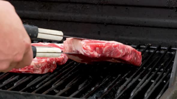 A raw rib eye steak is placed on a grill next to another one.