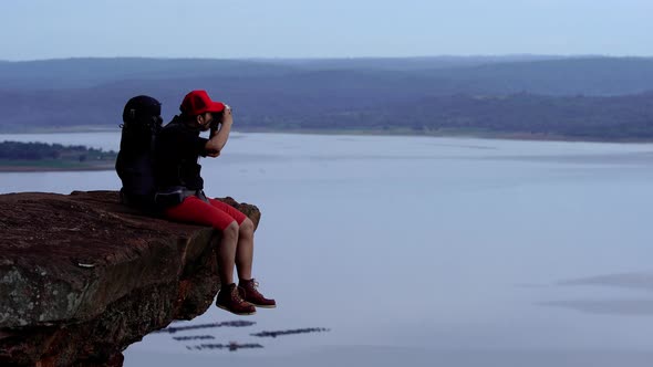 man traveler with backpack using camera taking a photo on the edge of cliff