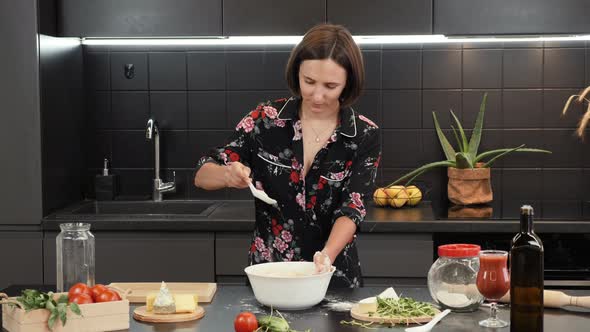 Female cooking in home modern kitchen, preparing pizza for family, adding and mixing ingredients.