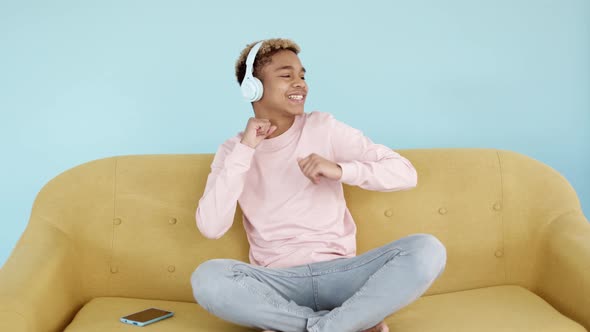 Happy Young Man Dancing While Listening to Music with Headphones Sitting on Sofa