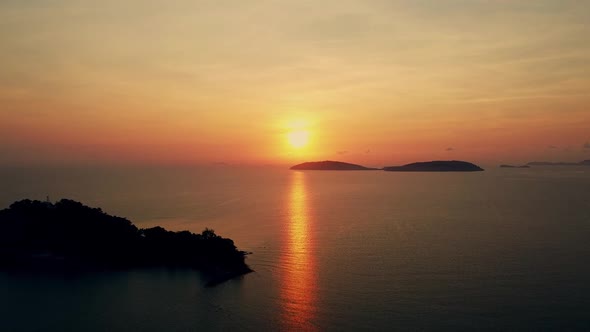 Aerial view of a beautiful sunrise behind the mountains island over the ocean and flying smooth over