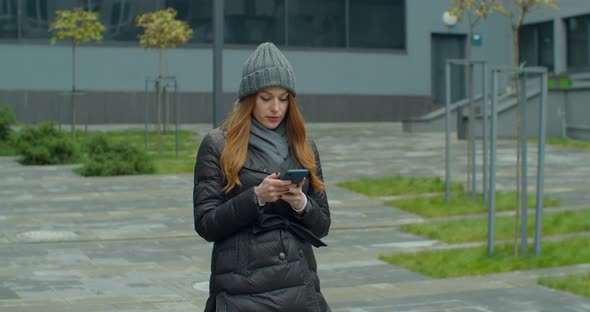 Portrait of Woman in a Hat Typing By Mobile Phone Outdoors. Close Up Cheerful Girl Walking