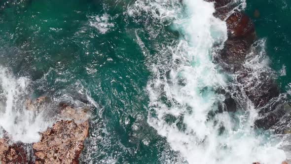 Top-down view of azure ocean waves and stone shore with sea turtles swimming (Kauai, Hawaii, USA)