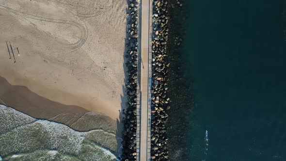 A recently constructed concrete walkway dividing a boating channel and popular surfing beach. High d