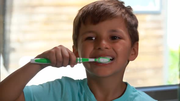 Little Cheerful Boy in a Blue Tshirt is Brushing His Teeth in the Bathroom