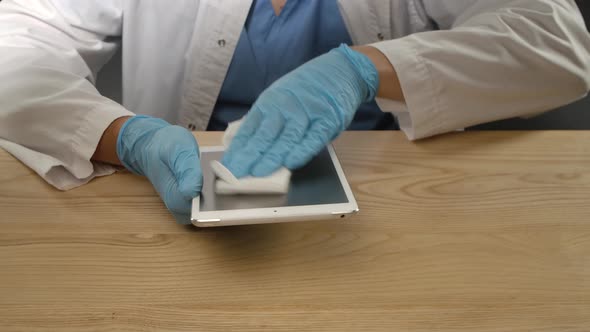 Prevention of Coronavirus. A Man in a Protective Medical Suit Wipes a Tablet with an Antibacterial