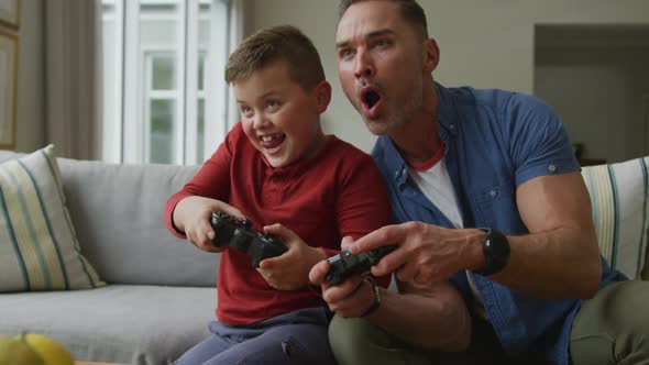 Happy caucasian father with son sitting in living room and playing video games