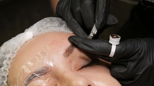 Beautician in Black Gloves Does Permanent Makeup Correction of the Shape of the Eyebrows to Young