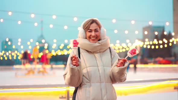 Woman in Earmuffs Standing Outdoor Near Ice Skating Rink on Central City Square at Winter Holiday