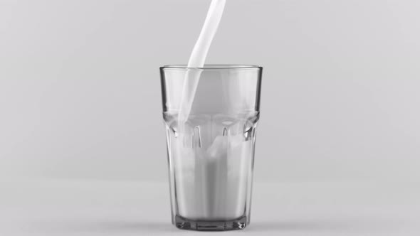 Milk Pouring Into Faceted Glass Close Up Isolated on Light Grey Background