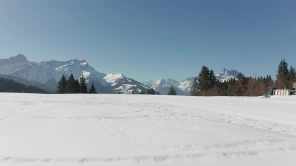 low Aerial of snow covered field, drone quickly ascending over beautiful valley with pine tree fores