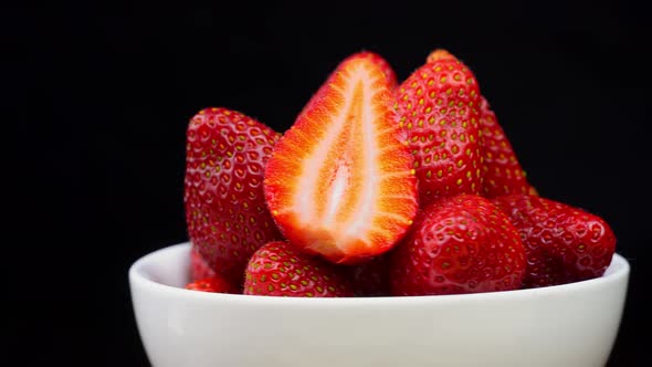 Strawberries without tails lie in white bowl or plate. It rotates