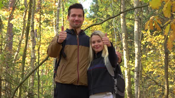 A Hiking Couple Shows a Thumb Up To the Camera with a Smile in a Forest on a Sunny Day