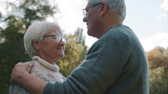 Happy Old Couple Dancing at Autumn Park. Senior Man Flirting with Elderly Woman. Kiss in Forehead in