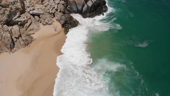 Aerial View of Waves Crashing onto Beach Alongside Rock Formation