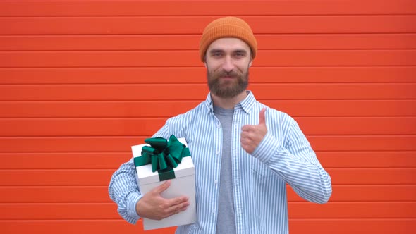 Handsome Young Hipster Holding Gift Box on a Red Background. Concept of Holidays and Birthdays