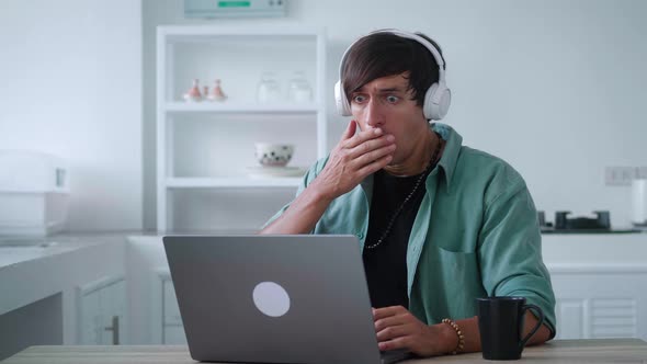 Scared Young Man in Headphones Getting Bad Results on Computer at Home Office