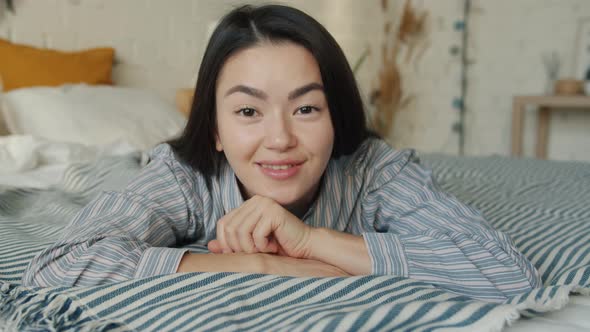 Portrait of Beautiful Asian Student Lying in Bed Smiling and Looking at Camera