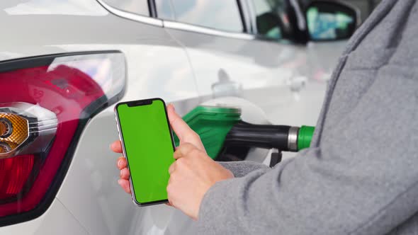 Woman Uses a Mobile Application in a Smartphone To Pay for Refueling a Car. Smartphone with a Green