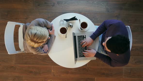 Two Business People in a Restaurant Working, Man Using Laptop, Woman Drinking Coffee