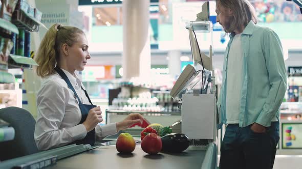 Female Cashier at Work in an Organic Store Man is Pays at the Checkout of the Grocery Store with Nfc