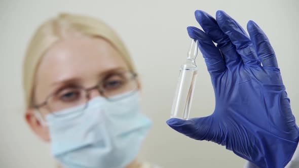 A Doctor in a Medical Mask Holds a Glass Ampoule with a Special Drug in Front of His Face