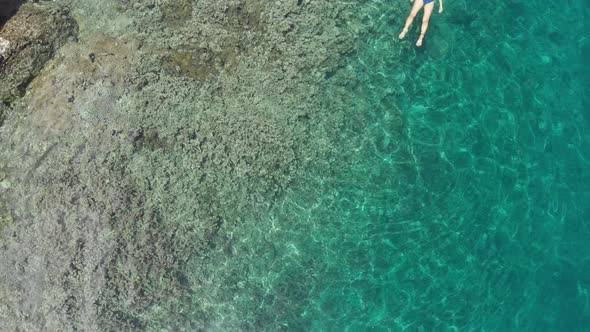 Aerial: woman snorkeling on Pulau Gunung Api coastline coral reef tropical